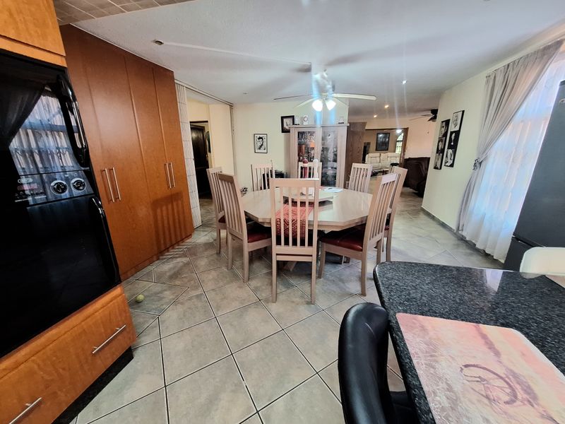 Open-plan dining and kitchen area featuring tiled flooring, built-in wooden cabinetry, granite countertops, and a ceiling fan.