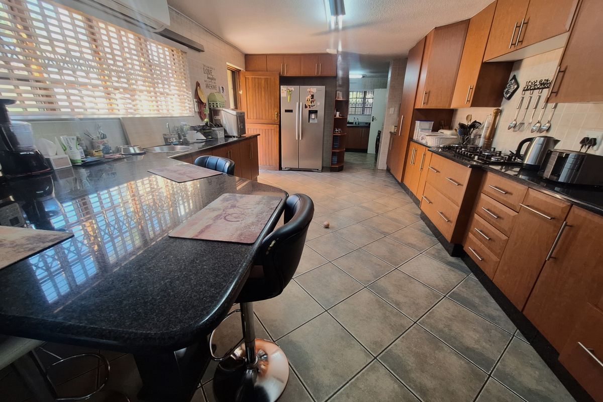 Spacious kitchen featuring wooden cabinetry, granite countertops, gas hob, and tiled flooring, with an adjoining scullery area visible in the background.