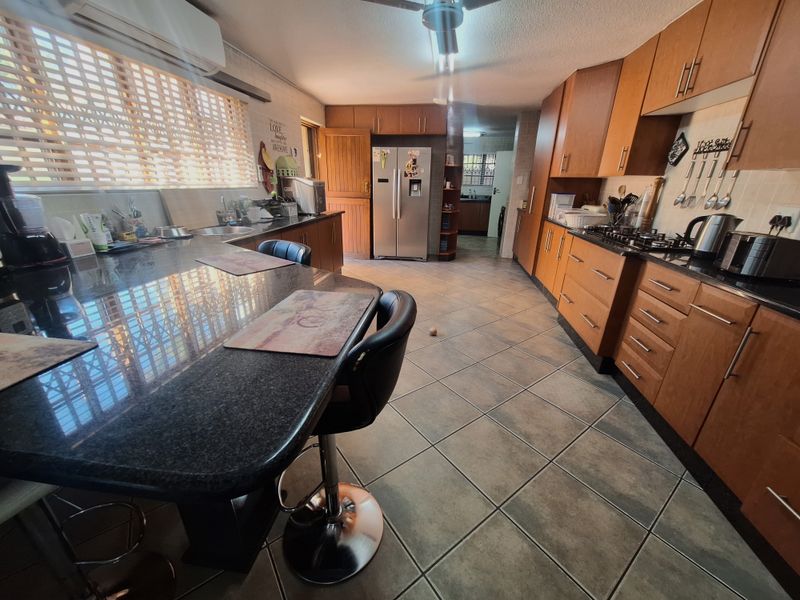 Spacious kitchen featuring wooden cabinetry, granite countertops, gas hob, and tiled flooring, with an adjoining scullery area visible in the background.
