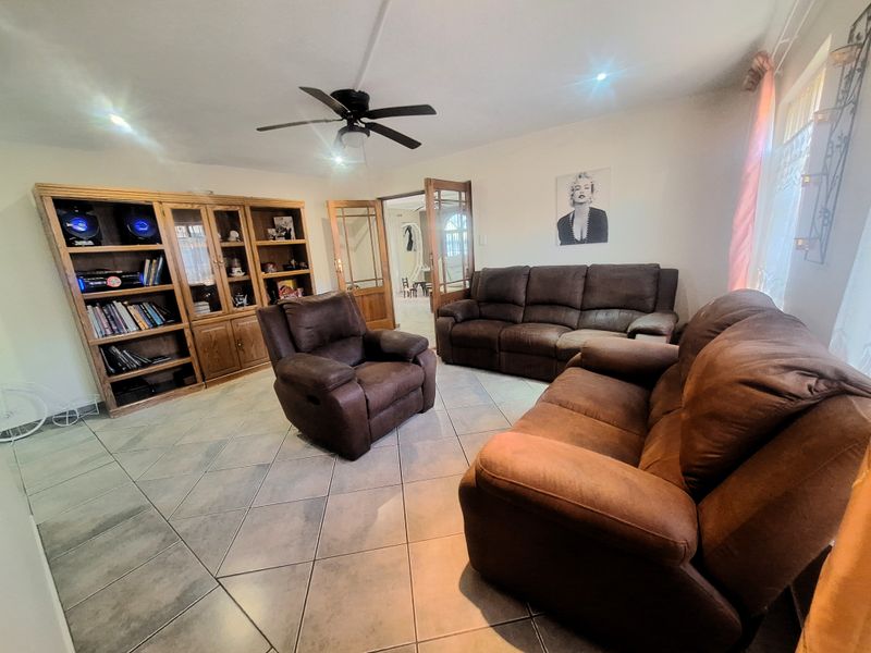 A living room featuring tiled flooring, a ceiling fan, and a built-in wooden shelving unit, with access through classic french doors.