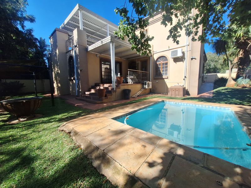 Rear view of the property featuring a swimming pool, stone-paved surround, and a covered patio area with an elevated balcony above.