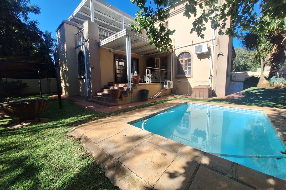 Rear view of the property featuring a swimming pool, stone-paved surround, and a covered patio area with an elevated balcony above.
