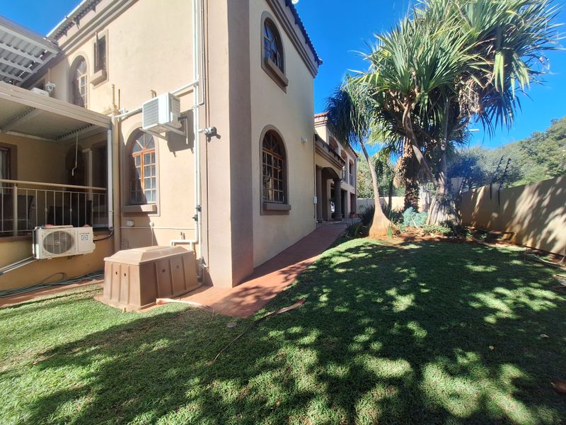 Rear exterior view of the house featuring a paved walkway, landscaped garden, and wall-mounted air conditioning units.