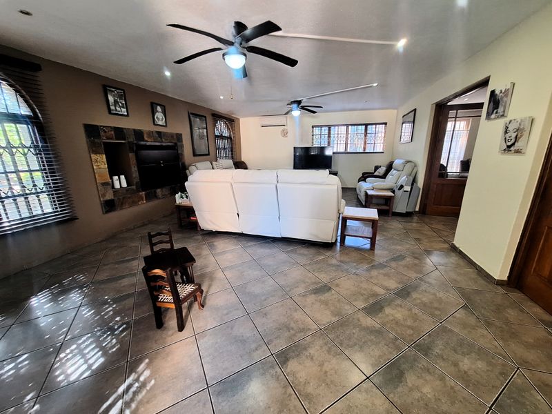 Spacious living room featuring ceramic floor tiles, a stone-clad fireplace, ceiling fans, and split-system air conditioning, offering a comfortable and functional layout.