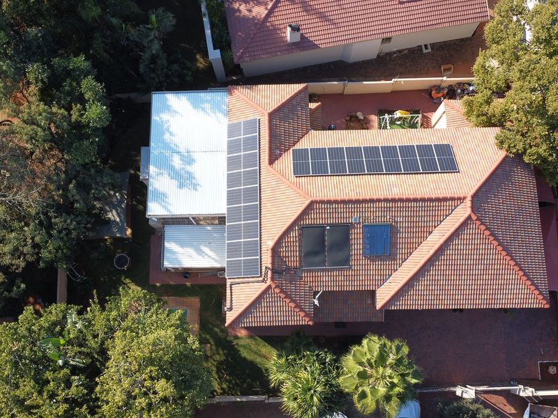 Aerial view of the property showcasing the tiled roof, integrated solar panel array, solar water heating system, and surrounding garden area.