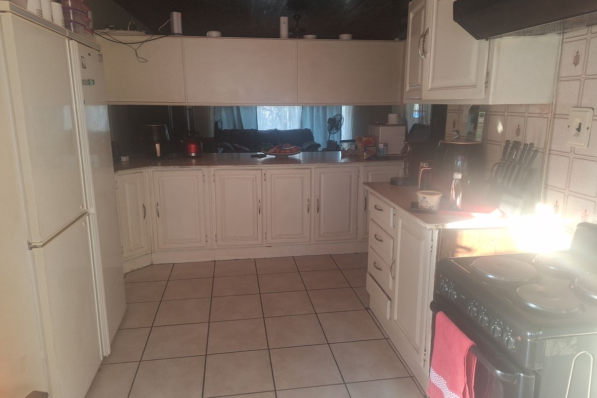 A dated kitchen featuring white cabinetry, tiled splashbacks, and tiled flooring, with a built-in stove and extractor fan.