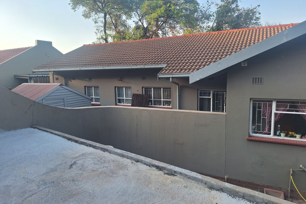 Exterior view of the property showing the rear facade, tiled roof, security bars on windows, and a concrete patio area.
