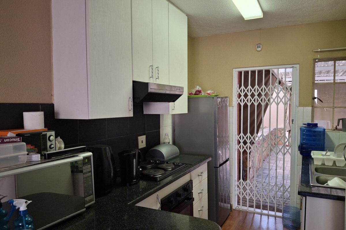 Functional kitchen featuring dark granite countertops, white cabinetry, built-in hob, extractor fan, and direct access to an outdoor patio area through a security gate.