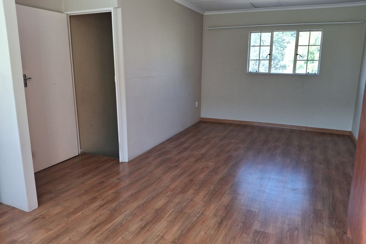 A vacant bedroom featuring laminate wood flooring, neutral wall tones, and a window providing natural light.