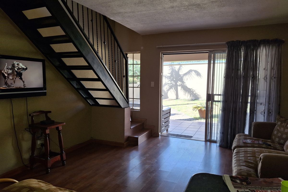 Living room featuring laminate flooring, a metal staircase with decorative railing, and sliding glass doors providing access to the rear patio and garden.