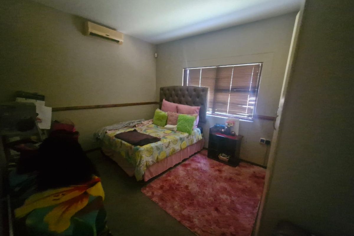 A bedroom featuring a wall-mounted air conditioning unit and wooden window blinds.
