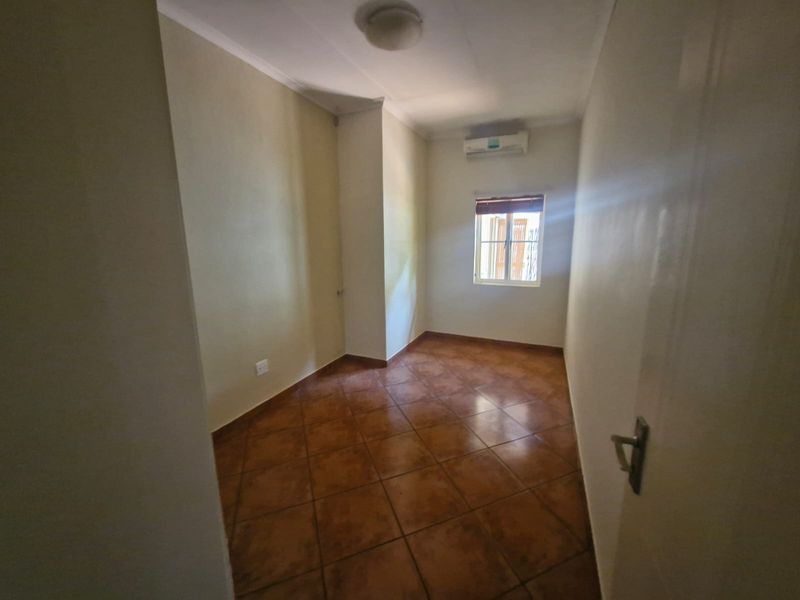 A vacant bedroom featuring tiled flooring, an installed air conditioning unit, and a window fitted with security bars.