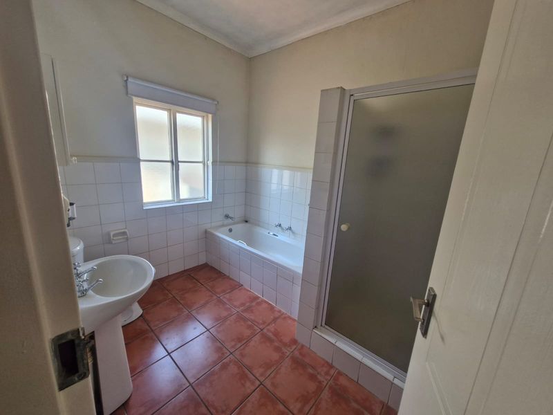 A functional bathroom featuring a pedestal basin, built-in bathtub, and a separate shower enclosure with tiled finishes.