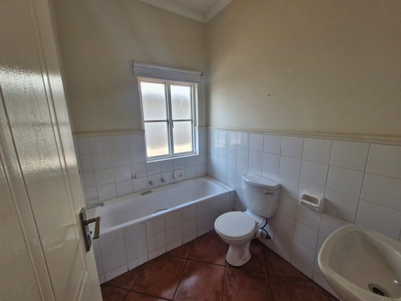A functional bathroom featuring a built-in bathtub, toilet, and pedestal basin with classic white wall tiling and terracotta-style floor tiles.