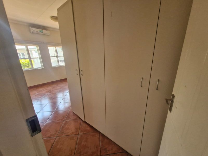 A bright, empty bedroom featuring tiled flooring, built-in cupboards, and a wall-mounted air conditioning unit.