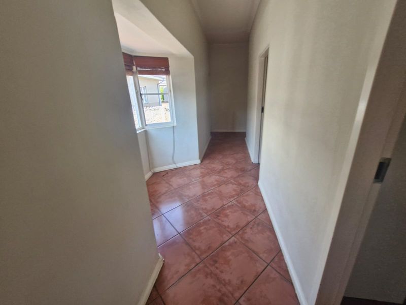 A vacant hallway featuring terracotta-style floor tiles and a bright bay window, providing access to adjacent rooms.