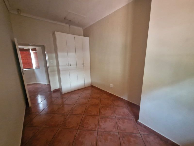 An empty bedroom featuring tiled flooring and a built-in wardrobe, with a doorway leading to an adjacent space.
