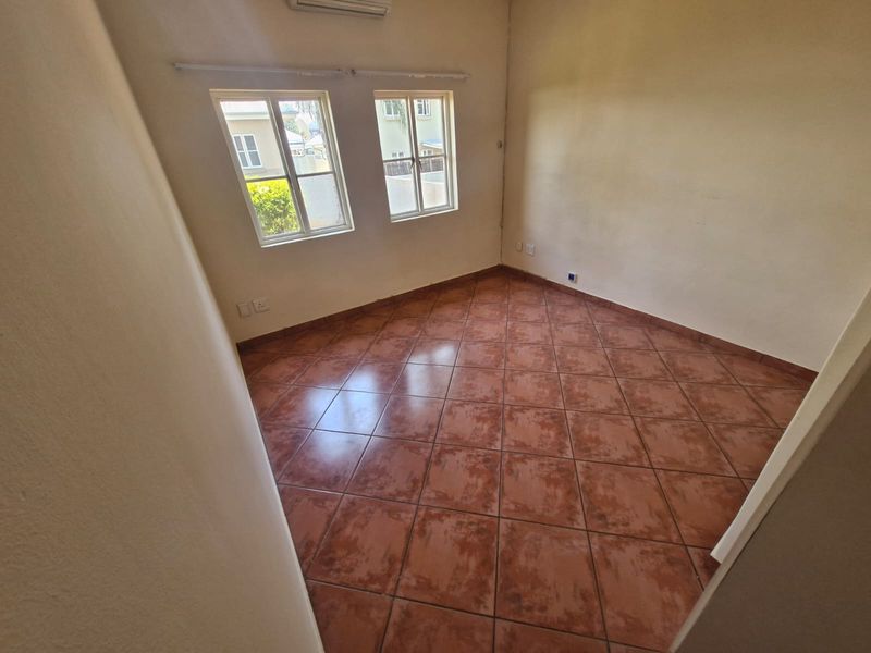 An empty bedroom featuring tiled flooring, a wall-mounted air conditioning unit, and dual casement windows providing natural light.