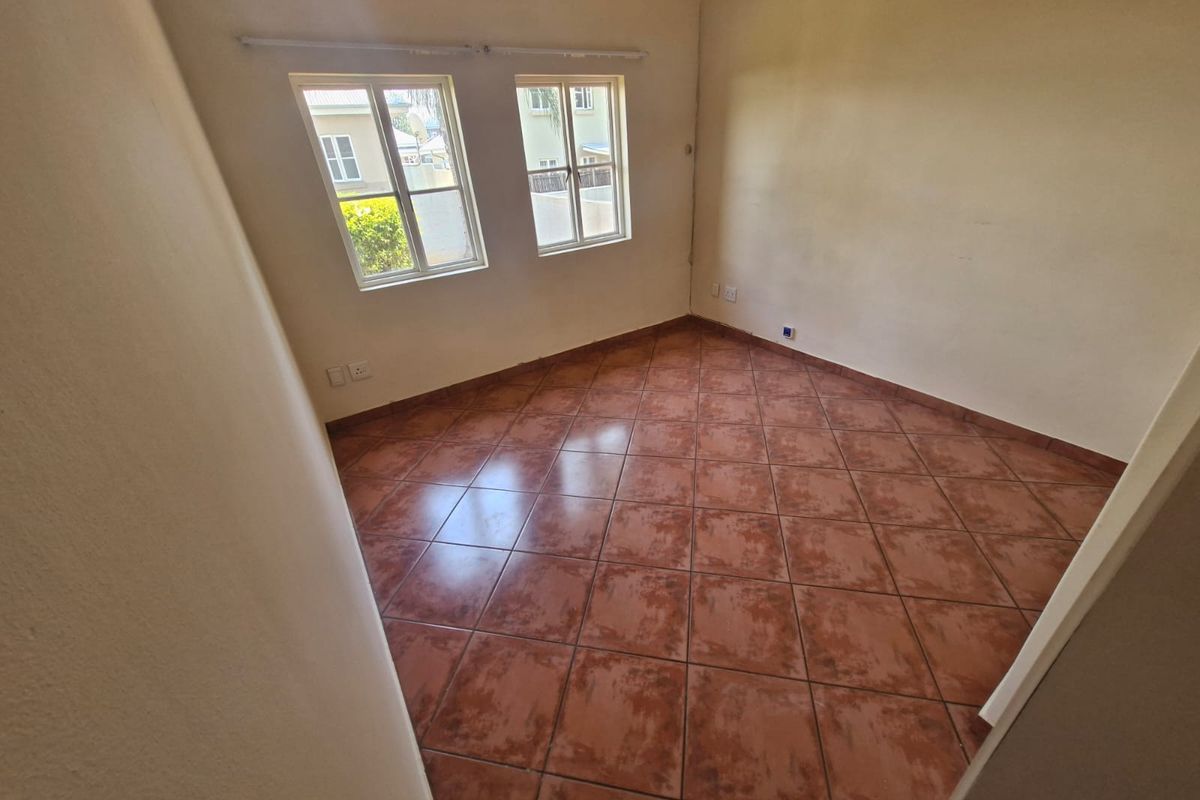 An empty bedroom featuring tiled flooring, a wall-mounted air conditioning unit, and dual casement windows providing natural light.