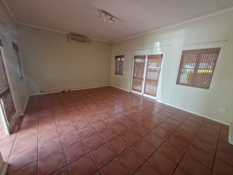 Spacious, empty living area featuring terracotta-style floor tiles, a wall-mounted air conditioning unit, and direct access to the exterior through double glass doors.