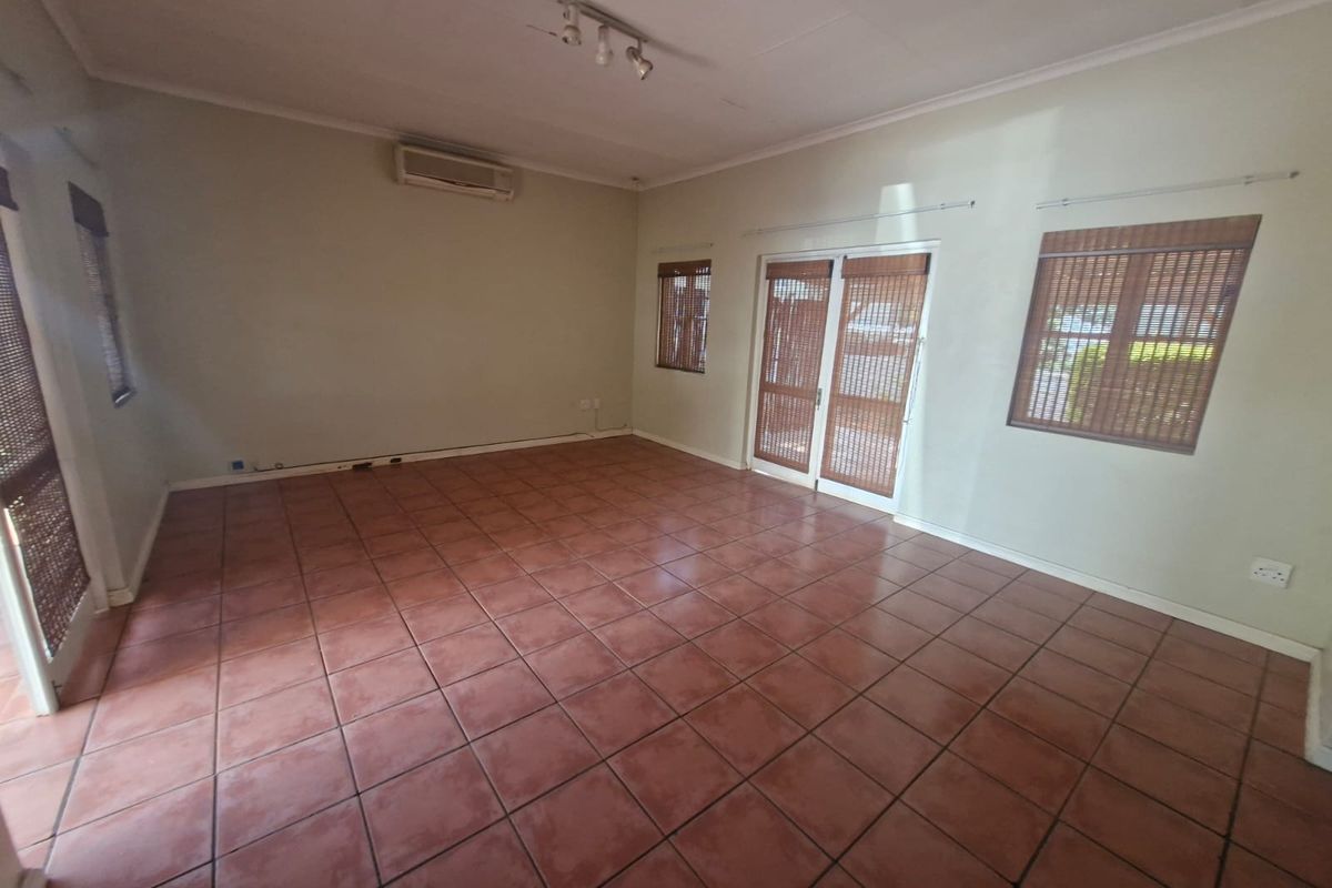 Spacious, empty living area featuring terracotta-style floor tiles, a wall-mounted air conditioning unit, and direct access to the exterior through double glass doors.