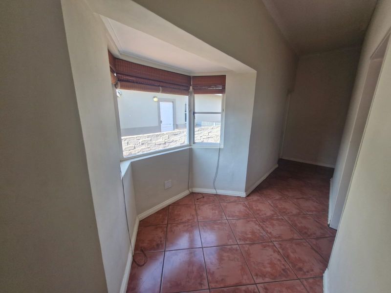 An empty living area featuring a bay window, ceramic tile flooring, and coved ceilings, offering a bright and versatile space.