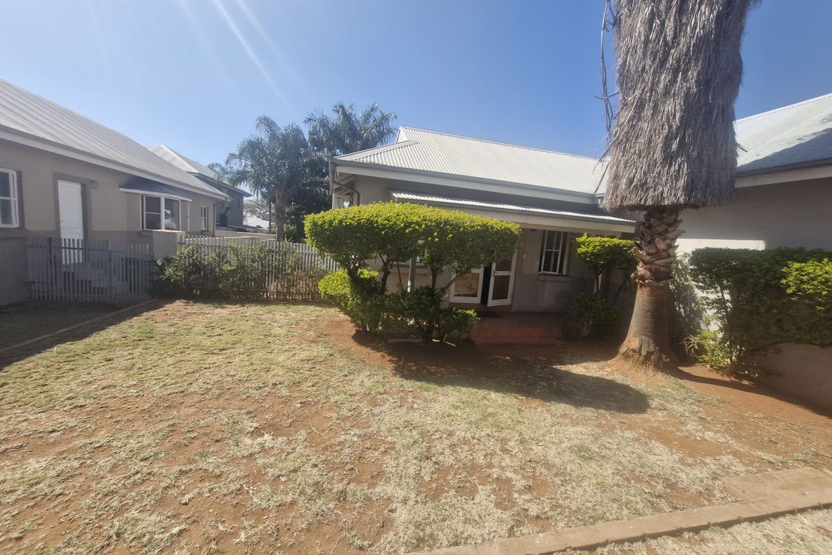 Rear view of the townhouse featuring a private garden area with a lawn, mature palm tree, and perimeter fencing.