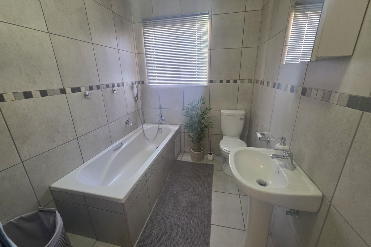 A functional bathroom featuring a bathtub, pedestal basin, and toilet, finished with neutral wall and floor tiling.