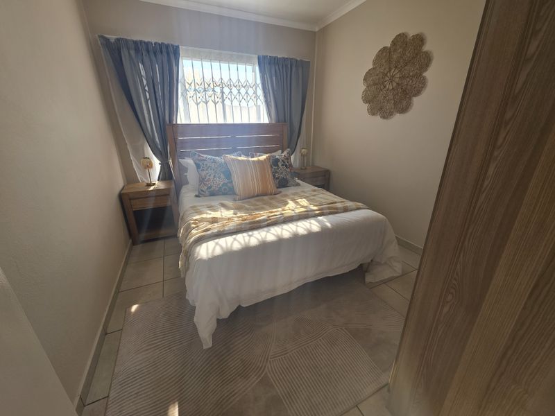 A compact bedroom featuring tiled flooring, a window with a security gate, and neutral wall finishes.