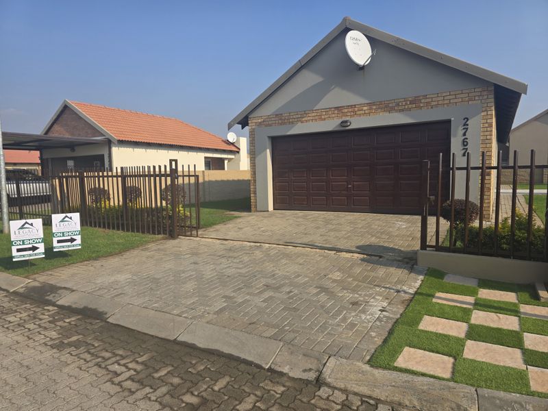 Front exterior view of a townhouse featuring a paved driveway, secure metal fencing, and a single-car garage with a sectional door.
