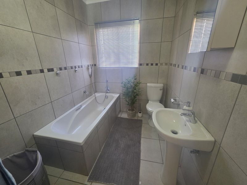 A functional bathroom featuring a bathtub, pedestal basin, and toilet, finished with neutral wall and floor tiling.