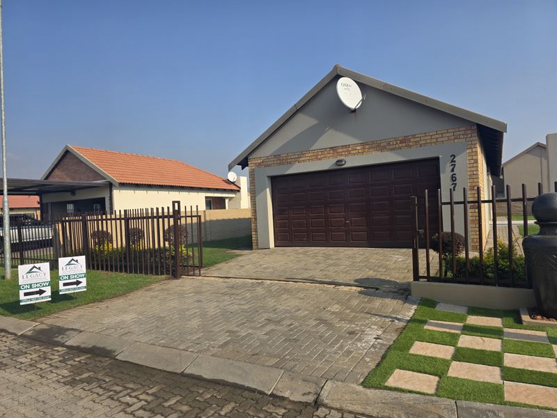 Front exterior view of a townhouse featuring a paved driveway, secure metal fencing, and a single-car garage with a gabled roof design.
