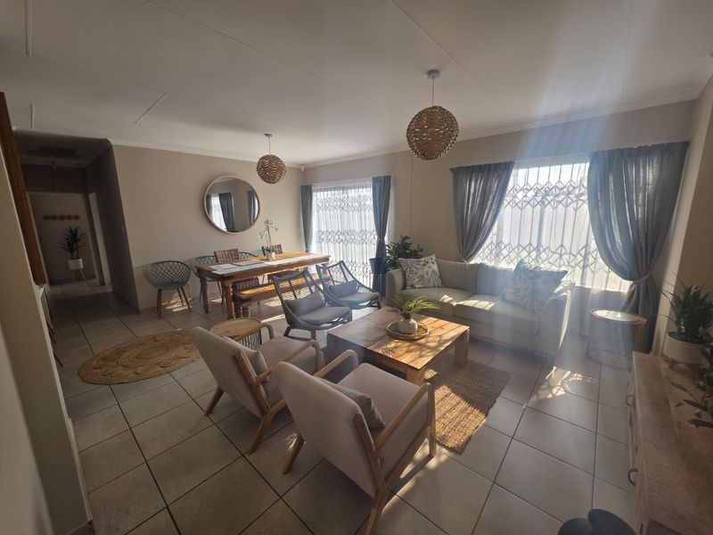 Spacious open-plan living and dining area featuring neutral wall tones, ceramic floor tiles, and large windows with security gates.