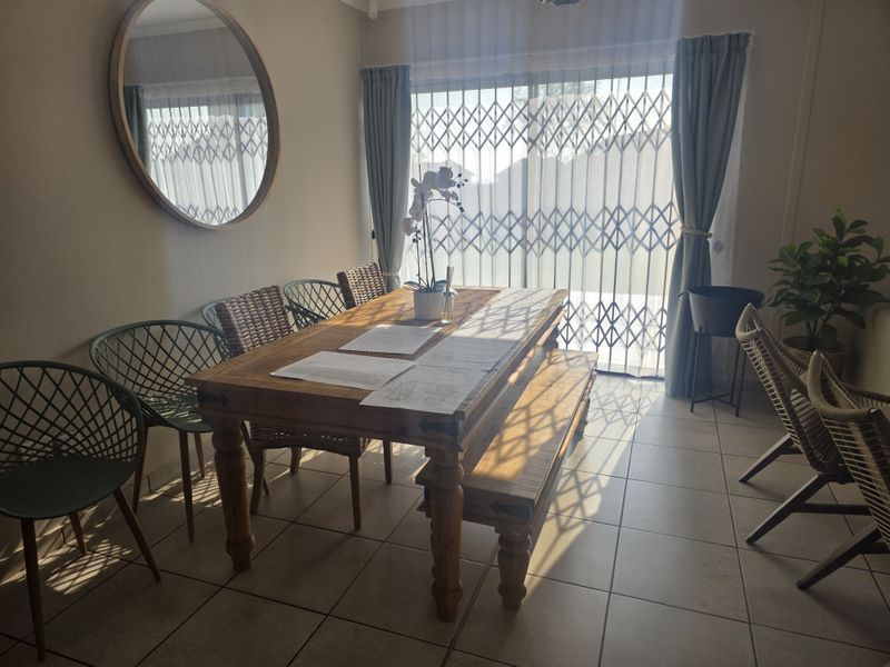 A bright dining area featuring tiled flooring and a sliding door with a security gate, allowing for natural light.