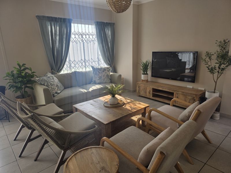 A well-maintained living room featuring tiled flooring, a security gate on the window, and a wall-mounted television setup.