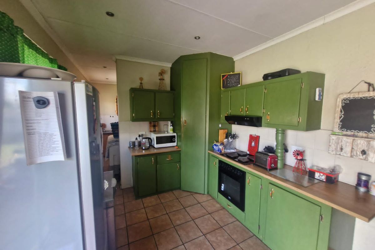 A dated kitchen featuring green cabinetry, built-in oven, extractor fan, and tiled flooring, offering a functional layout with potential for modernization.