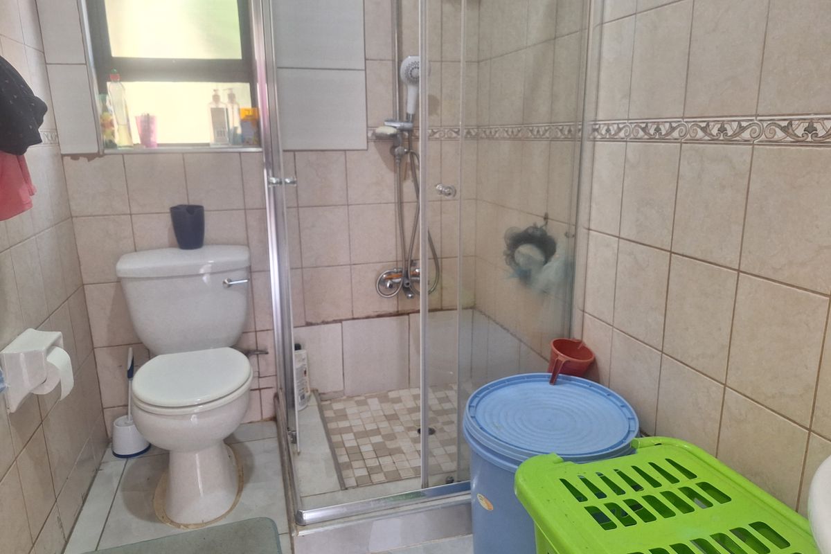 A functional bathroom featuring a glass-enclosed shower, ceramic wall tiling, and a standard toilet suite.