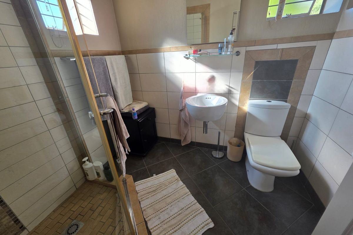 A functional bathroom featuring a shower enclosure, wall-mounted basin, and toilet with neutral wall and floor tiling.