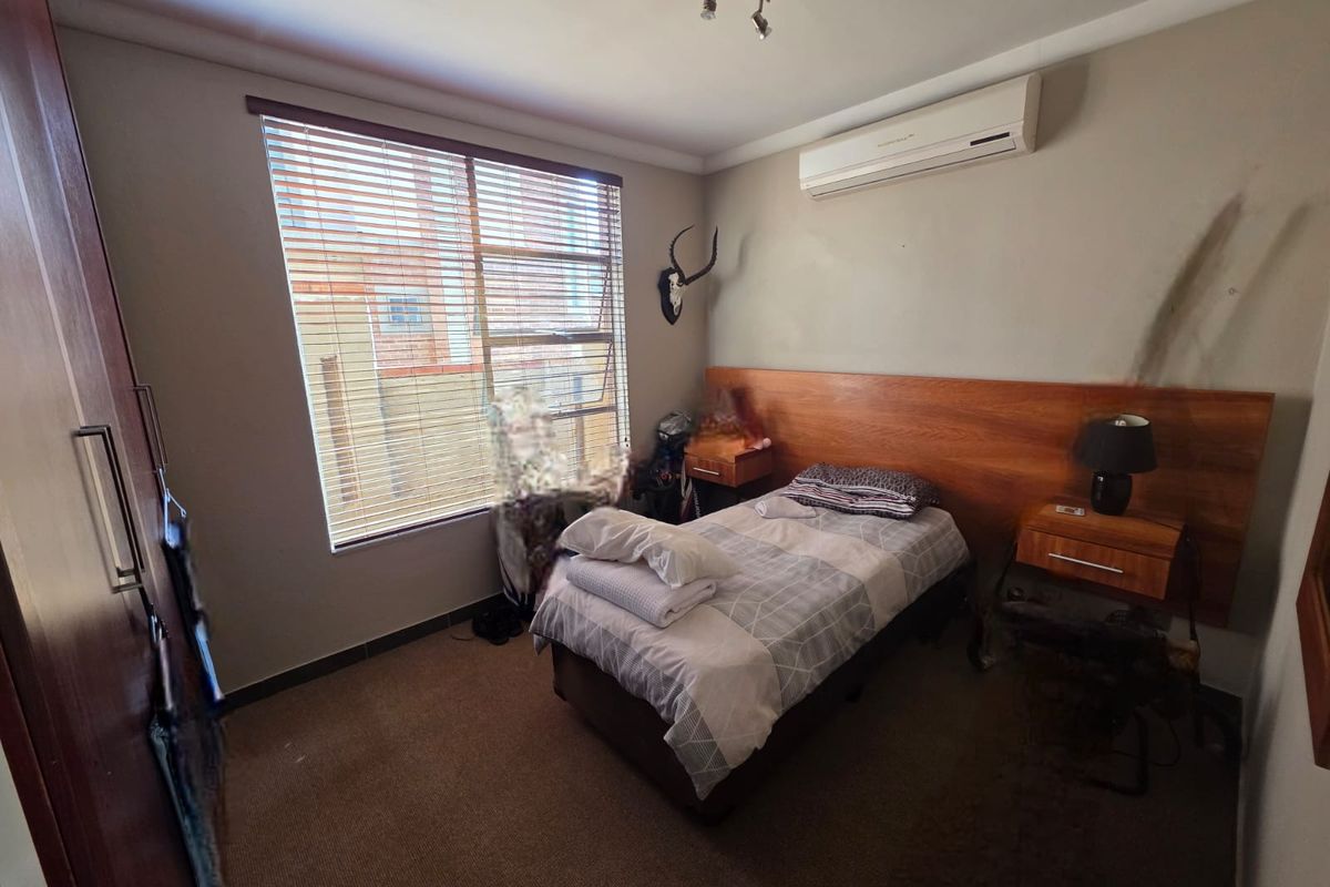 A functional bedroom featuring a built-in wooden headboard, air conditioning unit, and built-in cupboards with carpeted flooring.