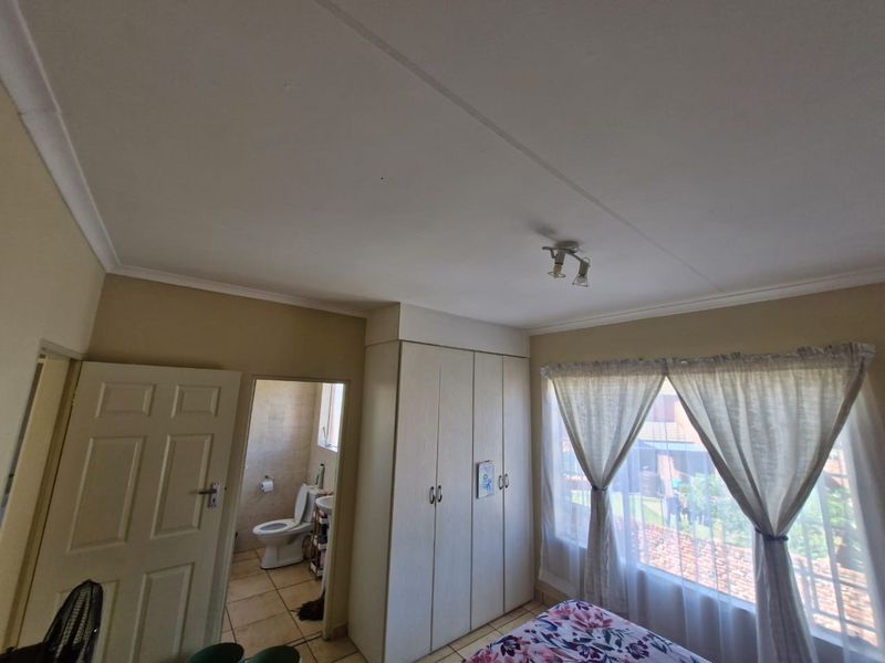 Bedroom featuring built-in cupboards and an attached en-suite bathroom with tiled flooring and natural light.