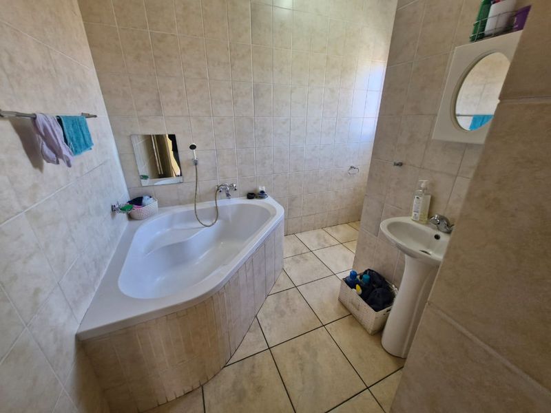 A functional bathroom featuring a corner bathtub, pedestal basin, and neutral floor-to-ceiling wall tiles.