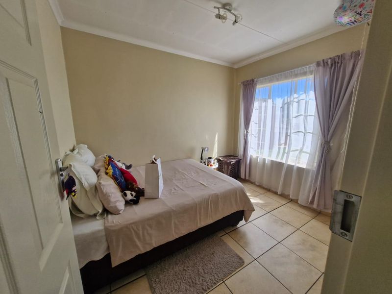 A functional bedroom featuring tiled flooring, neutral wall tones, and a large window allowing for natural light.