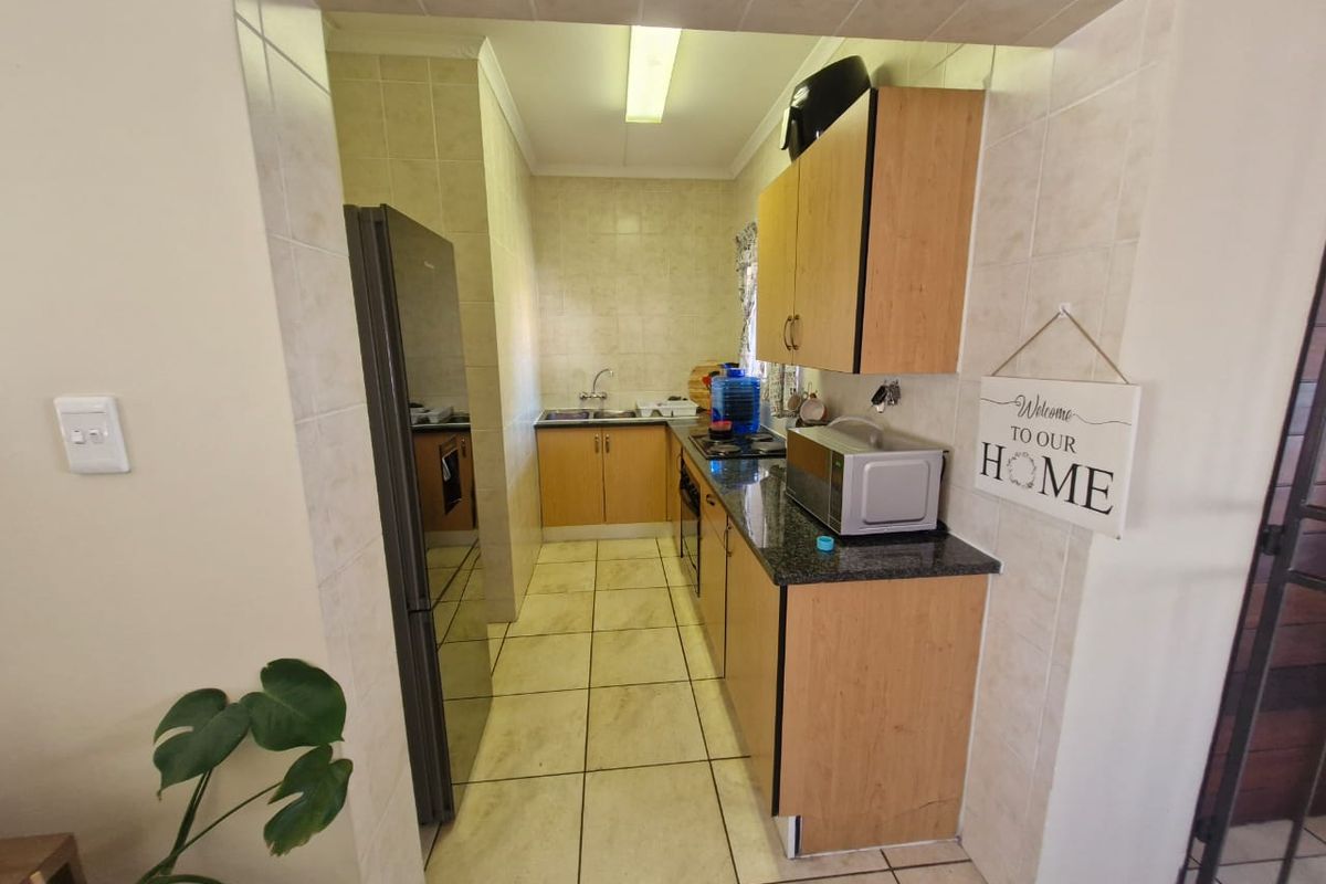 A functional galley-style kitchen featuring light wood cabinetry, granite countertops, tiled flooring, and a built-in oven and hob.