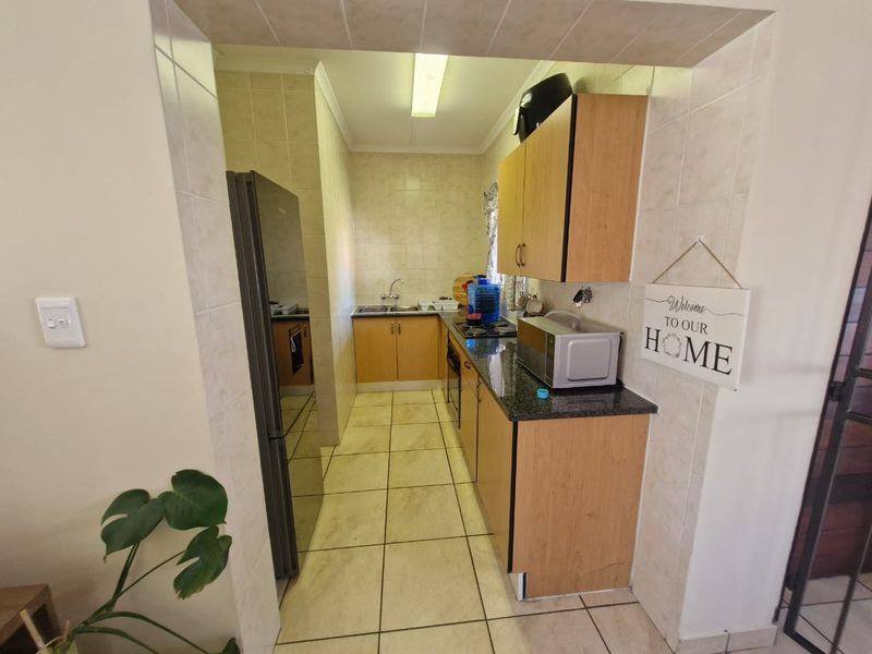 A functional galley-style kitchen featuring light wood cabinetry, granite countertops, tiled flooring, and a built-in oven and hob.