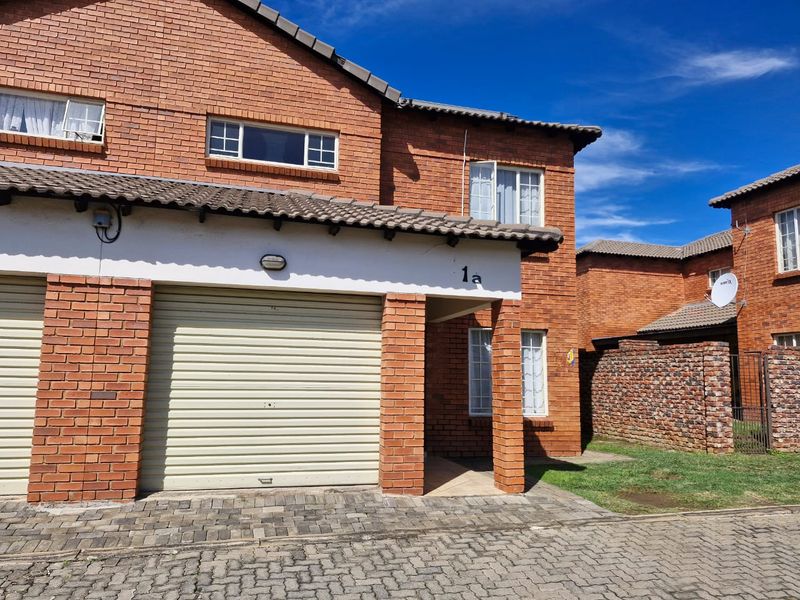Front elevation of a brick townhouse featuring a single roller garage door, covered entrance, and paved driveway area.