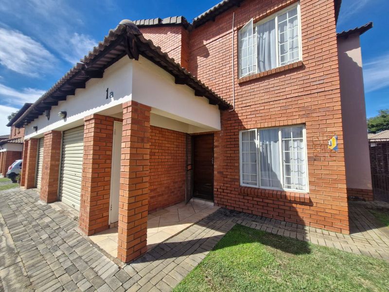 Front elevation of a double-story townhouse featuring a red brick facade, tiled roof, paved driveway, and a covered entrance with a garage.