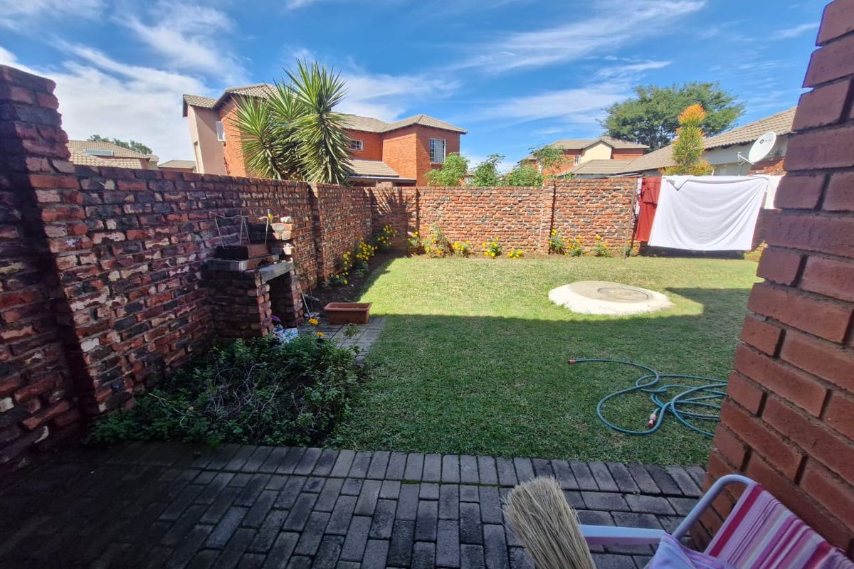 A private rear garden featuring a paved patio, built-in brick braai, and a lawn enclosed by high brick boundary walls.