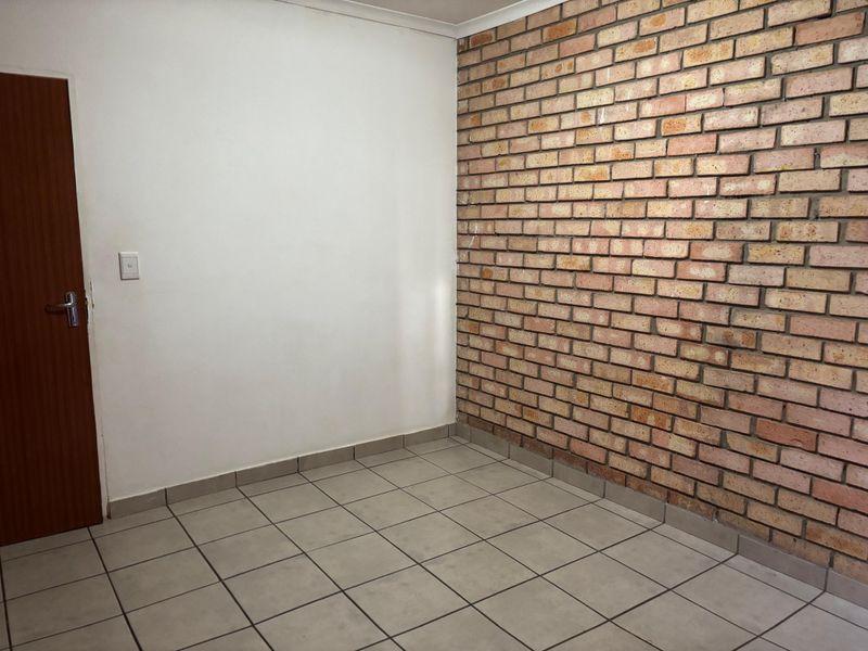 An empty bedroom featuring a rustic exposed brick feature wall, neutral ceramic floor tiles, and a solid wood door.