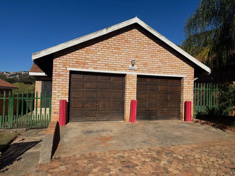 A detached double garage featuring a classic brick facade, two wooden garage doors, and a paved driveway area.