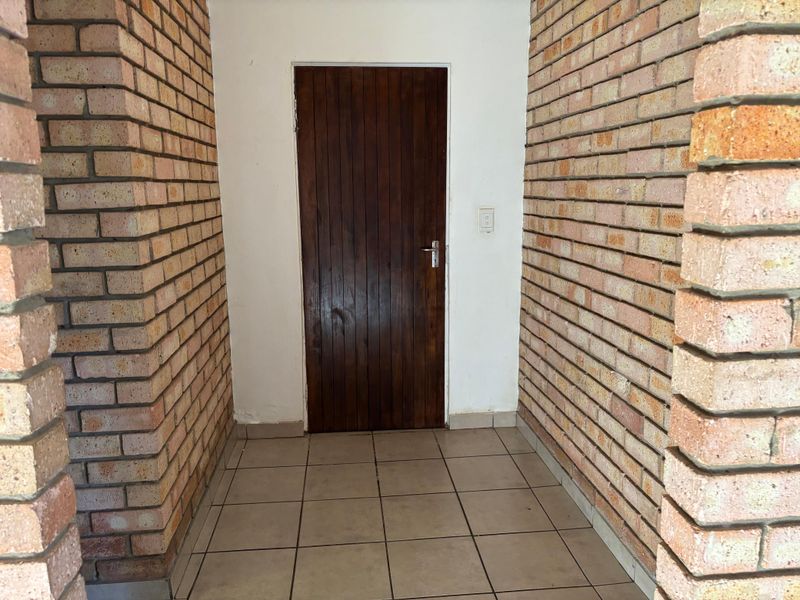 A simple entrance area featuring exposed brick walls, tiled flooring, and a solid timber door, offering a rustic foundation for potential cosmetic updates.